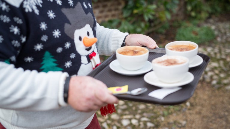 A man wearing a Christmas jumper carrying a tray of coffees